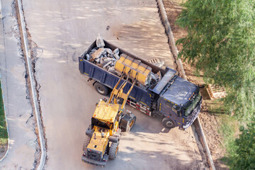 Aerial drone view excavator loading the tipper truck at the construction site under the tree