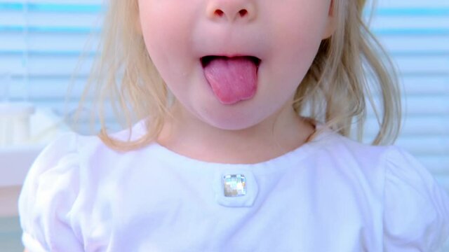 closeup mouth, part of the face of a small child, a blonde girl 2 years old in a white blouse smiles, performs exercises for the tongue, the concept of speech therapy, speech development