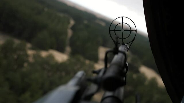 Chopper gun with round front sight sticking out of a hatch of a soaring helicopter in summer