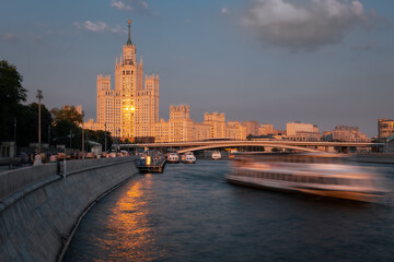 Fototapeta na wymiar Sunset cityscape featuring brightly lighted empire style skyscraper on a riverbank, Kotelnicheskaya embankment