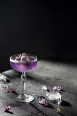 Beautiful purple cocktail in a crysral glass with gin,soda and ice ball frozen with gentle flowers on black background with flying drops and hard shadows.Drink in freeze motion.