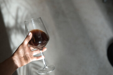 Woman hand holding wine glass, hot coffee pour over, steam. Sun lights and shadows concept, minimalism, hipster coffee shop, creative food photography. From above, overhead