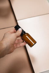 Woman hands holding brown glass bottle. Flatlay beauty skin care product still life on neutral paper background. Commercial studio shot, ad, minimalism concept, geometric lines, close up, mock up