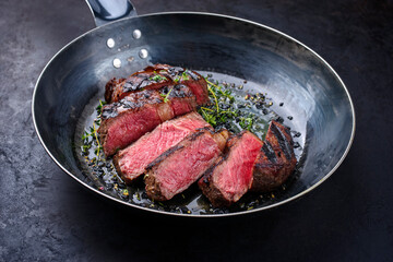 Traditional barbecue dry aged wagyu rib-eye beef steaks with herbs and black salt sliced and served as close-up in a wrought iron skillet on a black board