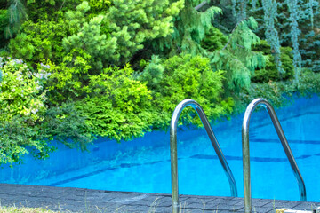 Metal railing with pool with blue water and green plants on the edge