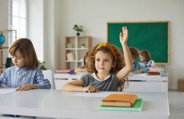 Elementary school student raises her hand, ready to answer the teacher's questions in class. Smart...