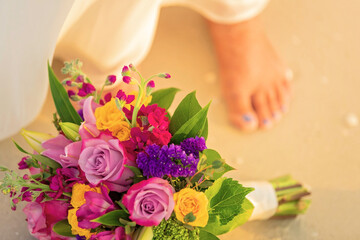 Closeup of wedding bouquet on the sandy beach with bride's foot out of focus in background