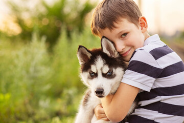 A little boy in a striped t-shirt lovingly hugs his pet husky dog outdoors © spyrakot