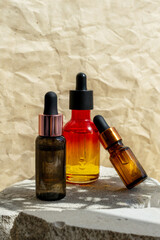Three Pipette Bottles Essential Oil, Serum mockup on grey stone podium, craft paper background. Beauty branding
