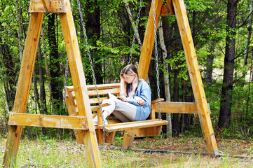 A teenage girl reads a book while sitting on a swing