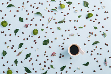 Coffee cup arranged with coffee beans and fresh flowers with foliage on a pastel blue background