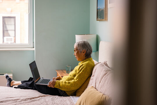 Senior woman using laptop while sitting in bedroom at home