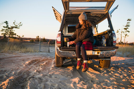 Young woman enjoying coffee in travel mug while beach car camping