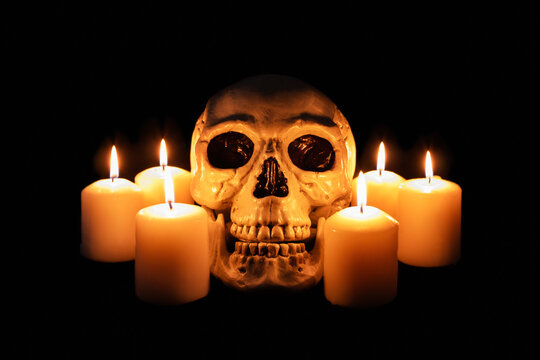 Human skull among burning candles in the dark, scary still life, altar