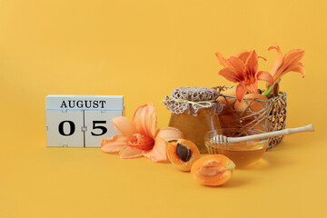 Calendar for August 5 : the name of the month of August in English, cubes with the numbers 0 and 5, honey, a jar of jam, apricots, daylily flowers on a yellow background.