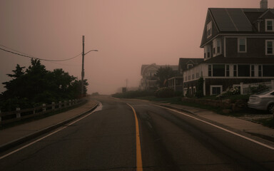 Foggy landscape of uphill road with trees and houses on Cape Cod coastline at Sunrise