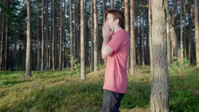 A young guy in a pink T-shirt walks and calls for help, forest