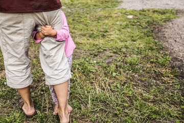 Children's hands hug father's leg in shorts in nature, close-up, frontal shooting, green grass on...