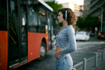 Young happy girl with curly hair walking on the street and listening music.