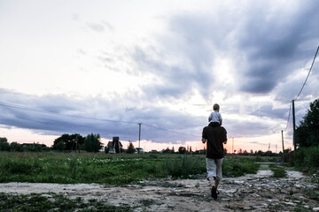 Father with his son sitting on his neck goes into the sunset, to the field, into the distance,...