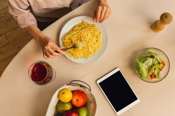 Mature senior woman in the kitchen preparing or eating tasty, homemade pasta in kitchen. Top view. Using tablet computer screen.