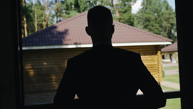 The silhouette of a guy standing on the porch and putting on a jacket. It's light outside and you can see the outline of his silhouette