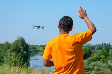 Young smiling African American man operating drone with controller standing with back and waving...