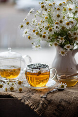 Hot chamomile tea in cup with flowers on wooden table.