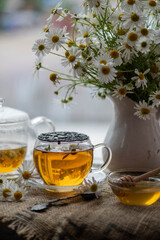 Hot chamomile tea in cup with flowers on wooden table.