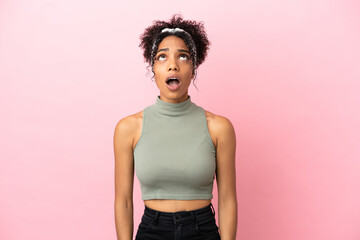 Young latin woman isolated on pink background looking up and with surprised expression