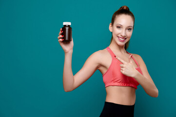 Smiling attractive female wearing sport fit holding a bottle with pills or drugs and show finger to...