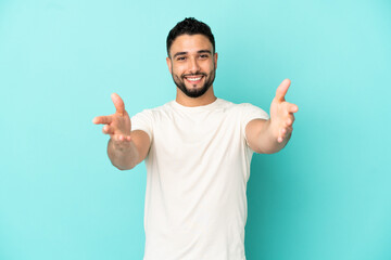 Young arab man isolated on blue background presenting and inviting to come with hand