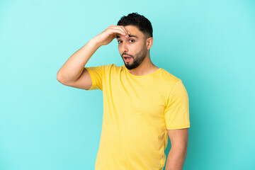 Young arab man isolated on blue background doing surprise gesture while looking to the side