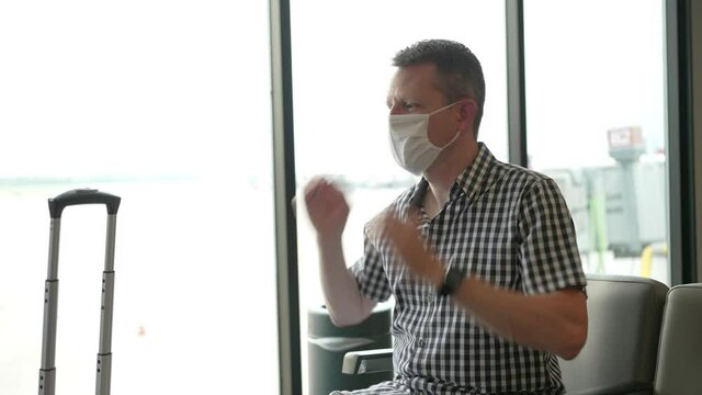 A traveling man at an airport gate puts a face mask on to wait for his airplane. Face masks were a common sight to stop the spread of COVID-19.  	