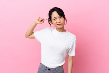 Young Vietnamese woman isolated on pink background making the gesture of madness putting finger on...