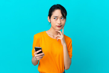 Young Vietnamese woman isolated on blue background using mobile phone and thinking