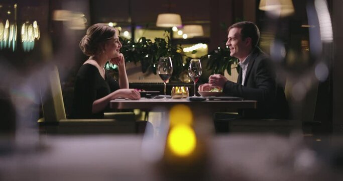 Joyful couple having a romantic dinner at a fancy restaurant. People enjoying their date, drinking wine, eating and chatting 4k footage