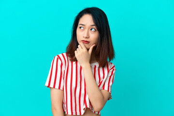 Young Vietnamese woman isolated on blue background having doubts