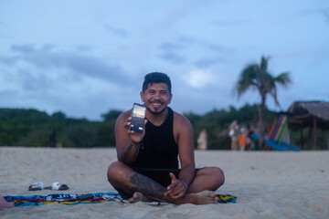 man smiles on the beach while showing off his cell phone