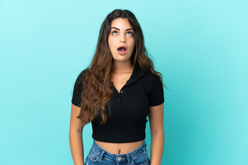 Young caucasian woman isolated on blue background looking up and with surprised expression