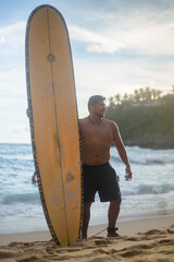 young man laughs on the beach with a surfboard at his side