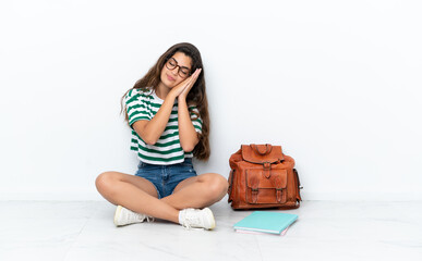 Young student woman sitting one the floor isolated on white background making sleep gesture in dorable expression