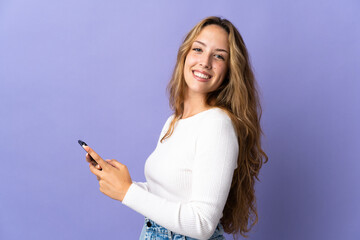 Young blonde woman isolated on purple background sending a message or email with the mobile