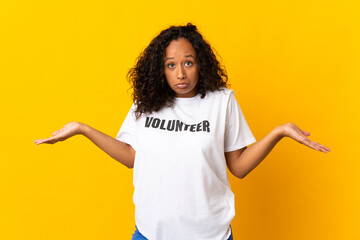 Teenager cuban volunteer girl isolated on yellow background having doubts while raising hands