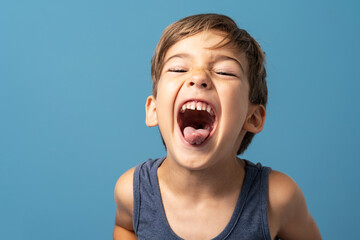 Front view of small caucasian boy four years old standing in front of blue background studio shot playful child making faces happiness and joy concept © Miljan Živković