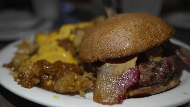 This mouth watering, panning video features a huge bacon burger with a side of chili cheese tots on a white plate at a restaurant.