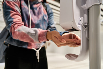 hands of an unrecognizable woman using an alcohol gel or hand sanitizer dispenser during the coronavirus or covid19 pandemic at the airport, new normal concept
