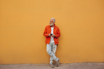 Full length portrait of man in orange jacket and jeans. Modern adult guy in bright clothes holds...
