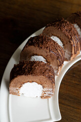 Chocolate roll with fresh cream on a white plate and wooden background