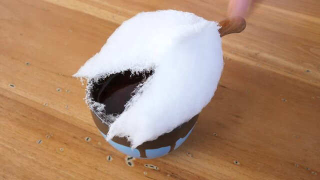 Top view of hands ripping cotton candy off and putting little wooden spoon into hot chocolate